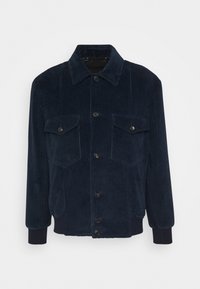 Granatowa kurtka z korduru z przodu zapinaną na guziki, dwiema kieszeniami na piersiach z klapkami, prążkowanymi mankietami i dołem oraz spiczastym kołnierzem.