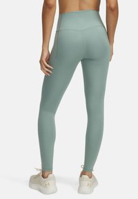 High-waisted, mint green leggings with a smooth finish and stitching details, paired with light-colored athletic shoes.