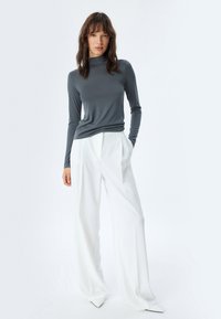 Grauer Langarmrollkragenpullover kombiniert mit weißen weit geschnittenen Hosen. Glattes Material mit einer figurbetonten Silhouette und subtiler Textur.