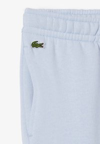 Pantalons de survêtement bleu clair en tissu doux avec une taille élastique, arborant un petit logo de crocodile vert sur le côté.