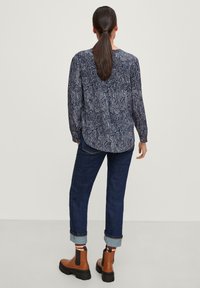 Blusa de manga larga en navy con un intrincado patrón blanco, combinada con jeans oscuros enrollados y botas de tobillo marrones con acentos negros.