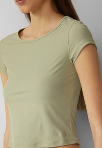 Lyhythihainen, vaaleanvihreä ribatutoppi, jossa on pyöreä kaula-aukko. Omistaa istuvan muotoilun ja huomaamattoman brändilogon helman lähellä. Pehmeä rakenne.