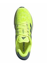 Baskets de sport jaunes vives avec une tige en mesh texturé, semelle grise, lacets proéminents et logo "Supernova" sur la languette.