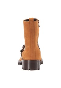 Cizmă din suede bej, până la gleznă, cu talpă plată maro, închidere cu fermoar pe lateral și o cataramă decorativă argintie pe partea exterioară. Textură netedă și formă dreaptă.