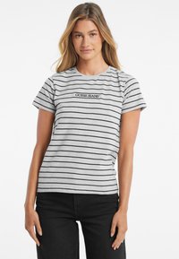 Pilkas ir juodas juostuotas marškinėliai su trumpomis rankovėmis, turintys centrini „GUESS JEANS“ logotipą. Pagaminti iš minkštos, pralaidžios medžiagos.