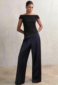 Schwarzes Off-Shoulder-Oberteil mit strukturiertem Muster und horizontalen Streifen, kombiniert mit lockeren, dunkelblauen weiten Hosen mit Nadelstreifen.