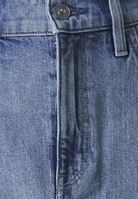 Jeans de mezclilla en azul claro, con cierre de botón, bolsillo frontal y costuras visibles. La tela presenta una textura suave y ligeramente descolorida.
