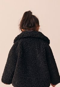Black fleece jacket with a textured, fluffy exterior, a large collar, and loose fit, shown from the back against a neutral background.