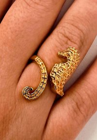 Arany, állítható gyűrű, amely egy részletes tengeri lóra hasonlít, egy ujjon, ahol a bőr textúrája is látható.