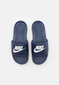 Sötétkék Nike papucsok texturált talpbéléssel, széles felső pánttal, amelyen fehér Nike logó látható, és formázott alakjukkal biztosítanak kényelmet.