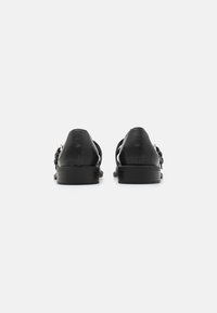Pantofi din piele neagră cu tocul jos, având un finisaj neted și un design tăiat pe lateral. Cusături subtile și accente de metal.