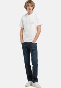 Witte katoenen T-shirt met grafische print, korte mouwen en ronde hals, gecombineerd met donkerblauwe denim jeans en witte sneakers.