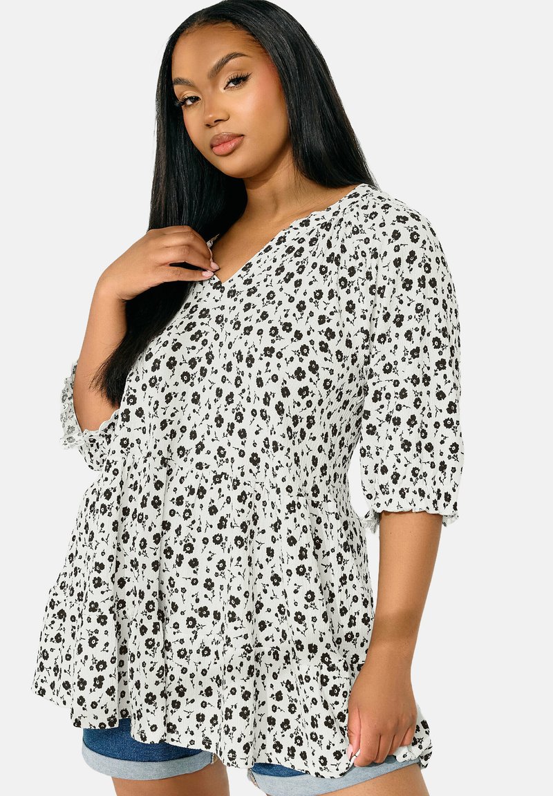 Vit blus med svart blommönster, V-ringning och trekvartsärmar, med en samlad midja och volangkant; lättviktig tyg.