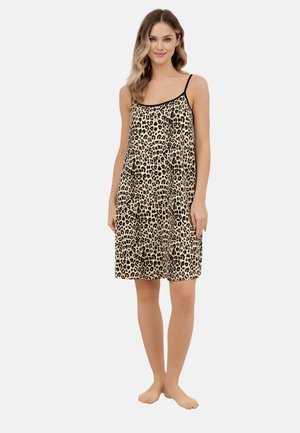 Kobieta stojąca boso, ubrana w sukienkę na ramiączkach z motywem panterki i cienkimi czarnymi paskami na białym tle.