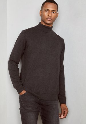 Chandail à col roulé gris foncé en tissu doux et texturé ; design ajusté avec des poignets et un ourlet côtelés, associé à un jean en denim foncé.