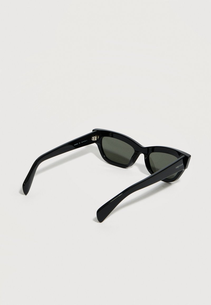 Schwarze rechteckige Sonnenbrille mit dunklen Gläsern, dicken Bügeln und dezentem Markenschriftzug an einem Bügel, dargestellt vor hellem Hintergrund.