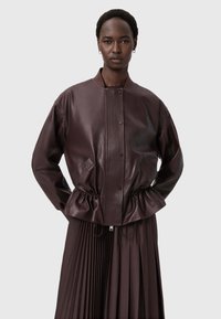 Hnědá kožená bombarďák s ribbeným předním panelem, řemínkem v pase a postranními kapsami, doplněná skládací sukní.