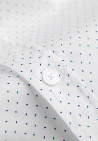 Camisa de tela blanca con un botón y un patrón de pequeñas formas en forma de gota en azul y verde. Textura suave con un diseño de cuello clásico.