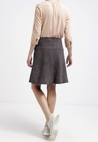 Jupe grise en daim en forme A avec une texture lisse, dotée d'une taille mi-haute et d'un design évasé. Portée avec un blouse beige clair et des chaussures blanches.