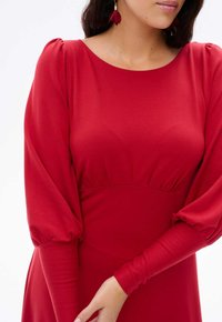 Czerwona sukienka z okrągłym dekoltem, z plisowanymi bufkami i dopasowanym korpusem, wykonana z miękkiej, gładkiej tkaniny, podkreślająca smukłą sylwetkę.