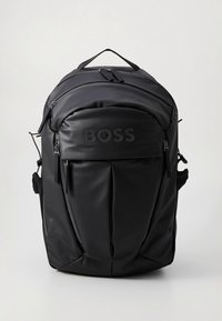 Svart ryggsäck med en jämn, matt yta. Har framficka med dragkedja, justerbara remmar, topphandtag och präglad logotyp på frampanelen.