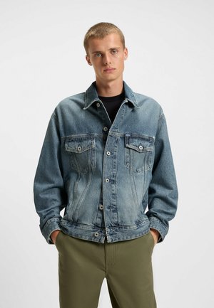 Denim jacket in faded blue with a button-up front, two chest pockets, and a classic collar. Features a relaxed fit and textured fabric.