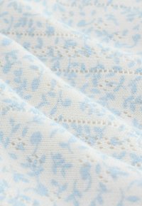 Tela ligera con una base blanca y un delicado estampado floral azul, tejido texturizado y secciones de punto abierto para mayor detalle.