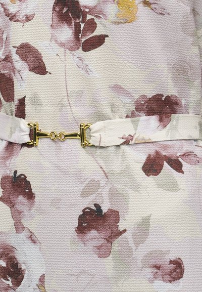 Κοντινό πλάνο ζώνης από ύφασμα με λουλουδάτο μοτίβο και χρυσό μεταλλικό κούμπωμα που κλείνει γύρω από αντίστοιχο ύφασμα.
