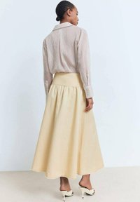 Gonna gialla chiara, alla lunghezza del ginocchio, con una silhouette svasata e una cintura arricciata. Abbinata a una camicia a righe a maniche lunghe e tacchi bianchi.