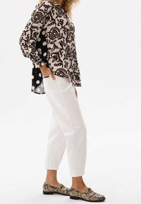 Blusa a motivi nera e beige con dettagli a pois, pantaloni bianchi a sigaretta e mocassini in stampa pitone, caratterizzati da una vestibilità rilassata e maniche lunghe.