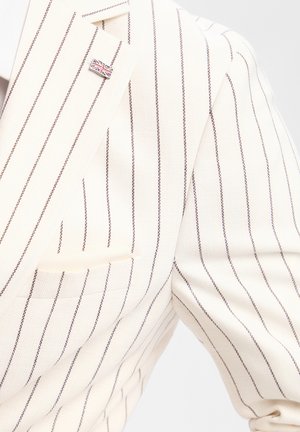 Veste blanche à fines rayures verticales noires avec une petite épingle drapeau Union Jack sur le revers gauche.