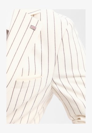 Veste blanche à fines rayures verticales noires avec une petite épingle drapeau Union Jack sur le revers gauche.