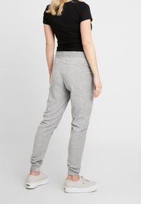 Grå mjukisbyxor i ett mjukt tyg, med elastisk midja och smalnande ärmslut, ihop med ljusa skor.