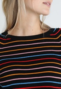 Mustapaita, jossa on vaaka-aitoja punaisena, vaaleanpunaisena, sinisenä, oranssina ja keltaisena. Paidan pinnassa on ribbitekstuuri ja pyöreä kaula-aukko.