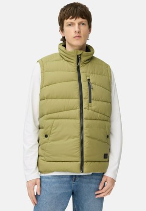 Padded olive green vest with a stand collar, front zip closure, two side pockets, and a textured finish. Worn over a white long-sleeve shirt.