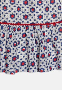 Tessuto floreale con fiori blu e centri rossi su uno sfondo bianco. Presenta un orlo arricciato con bordi rossi a onde.