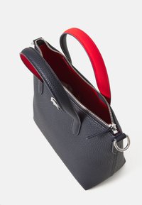 Borsa in pelle texturizzata blu con manico in tessuto rosso, chiusura con zip e finiture in argento. L'interno è rosso. Presenta un dettaglio con il logo iconico.