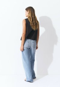 Black sleeveless top with scalloped edges paired with light blue, high-waisted denim jeans featuring side buttons and a relaxed fit.