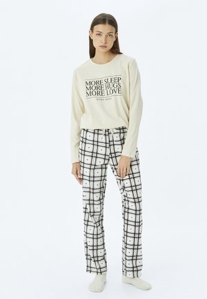 Camiseta de manga larga crema con texto negro; combinada con pantalones de cuadros en blanco y negro con cintura ajustable y textura de tela suave.