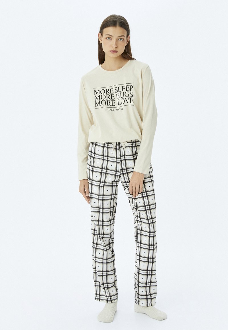 Cremfarbendes Langarm-T-Shirt mit schwarzem Text; kombiniert mit schwarz-weißen Karohosen mit Kordelzugbund und weichem Stoffgefühl.