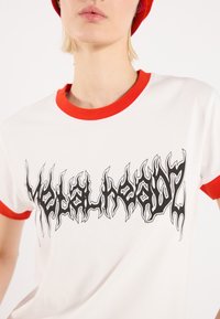 Bílý tričko s krátkým rukávem a červeným ribbovým límcem, s černým grafickým designem připomínajícím plameny a nápisem "Metalheadz."
