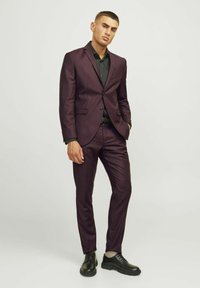 Costume violet foncé avec revers cranté, pantalon ajusté et chemise noire. Porté avec des chaussures noires. Texture lisse, design sur mesure.