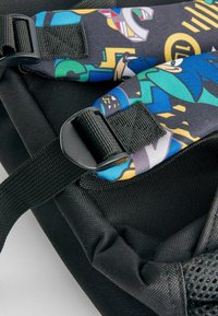 Svart tygryggsäck med färgglada mönstrade remmar som har tecknade figurer. Innehåller svart plastdetaljer och strukturerade material.