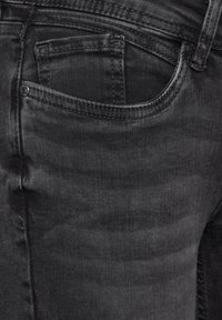 Černé džíny z denimu s úzkým střihem, s malou kapsičkou na mince vpředu a jemným vyblednutím. Švy jsou tmavé a rovnoměrné.