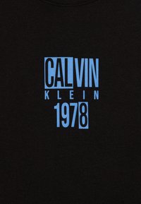 T-shirt in cotone nero con testo audace in azzurro chiaro: "CALVIN KLEIN 1978" in un layout geometrico e texture liscia.