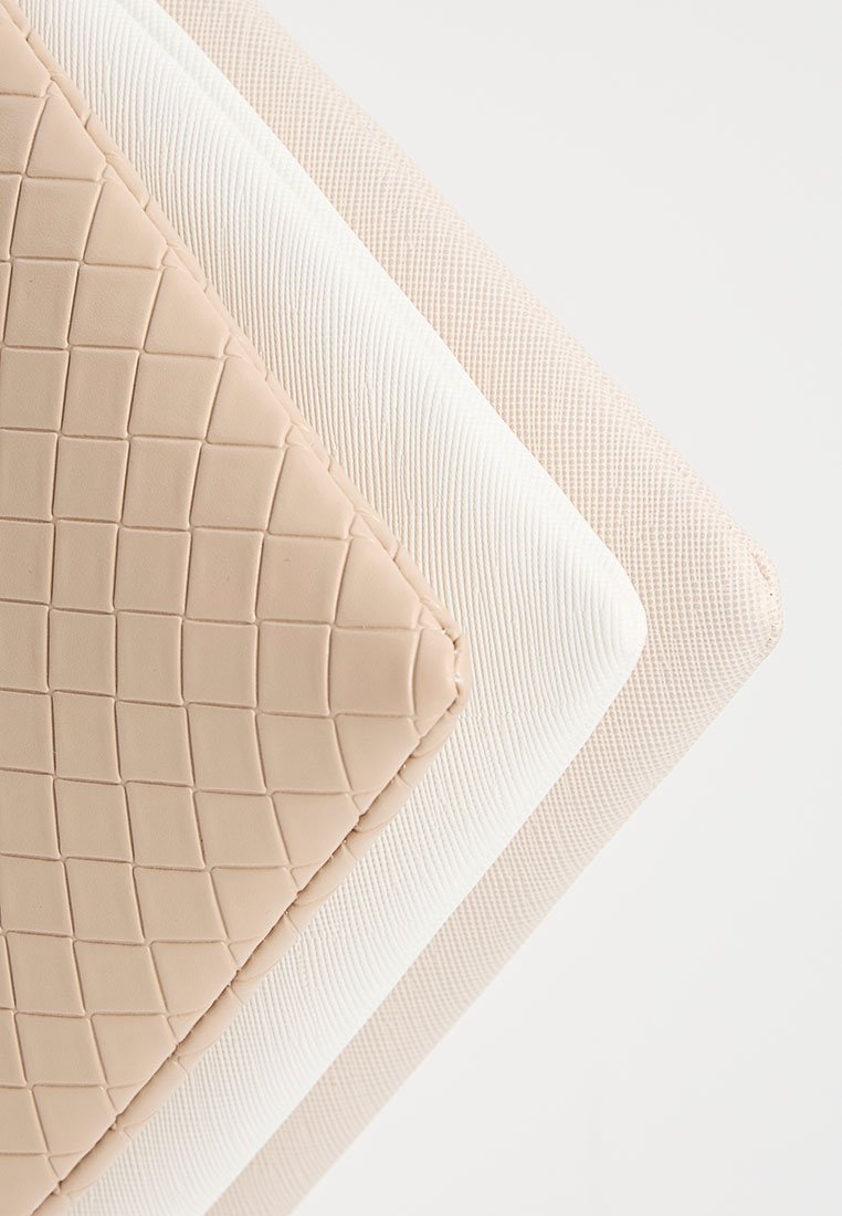 Drei gestapelte rechteckige Tischsets mit unterschiedlichen texturierten Oberflächen: gestepptes Beige, gerilltes Weiß und feines kariertes Beige.