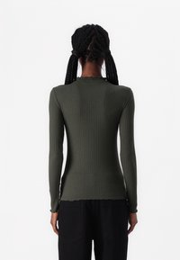 Ribbed long-sleeve top in olive green with a scalloped neckline and fitted style, paired with black pants. Smooth texture and stretchable fabric.