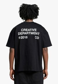 T-shirt nera in cotone con testo bianco stampato sul retro: "CREATIVE DEPARTMENT 2018 CD." Vestibilità ampia con maniche corte.