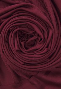 Burgundy fabric, rolled into a tight coil, features a subtle textured pattern. Smooth surface with soft, flexible material.