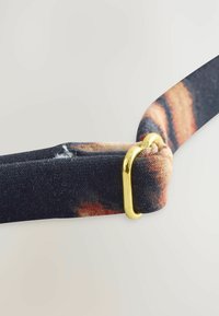 Textilný remienok v čiernej farbe s multicolor vzorom, vybavený zlatou kovovou prackou. Textúra sa zdá byť tkaná s viditeľným šitím a opotrebením.